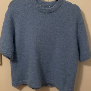 Blå stickad tröja från Gina Tricot - Mysig blå stickad tröja från Gina Tricot med kort ärm och rund halsringning. Tröjan har en enkel och clean look, perfekt att styla med jeans eller kjol. Materialet är mjukt och ger en chill vibe.