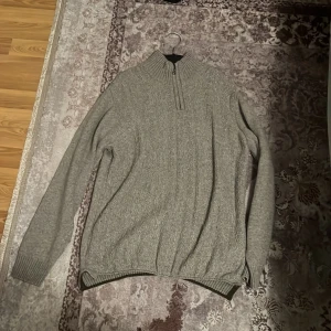 Grå stickad tröja från Kiğılı - Säljer en grå stickad tröja från Kiğılı i storlek L. Tröjan har ribbad hög krage med half zip och långa ärmar. Regular fit och snyggt diskret mönster längs hela tröjan. Perfekt för dig som gillar klassisk och enkel stil.