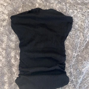 Svart bandeau tubtopp från H&M Divided - Svart bandeau tubtopp från H&M Divided i storlek S. Toppen är ribbad och har en tight passform som sitter snyggt runt kroppen. Perfekt att styla med jeans eller kjol för en cool och enkel look.
