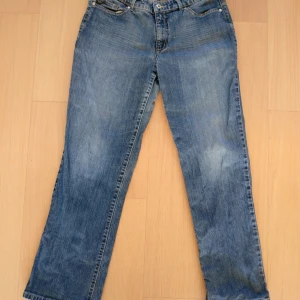 Blå jeans från Arizona med broderi, baggy - Säljer ett par blå jeans från Arizona med snyggt brunt broderi på bakfickorna. Jeansen har klassisk femficksdesign, raka ben och normal passform. Materialet är slitstarkt denim och färgen är mellanblå med lätt tvättad look. Slitna längst ner på byxbenen