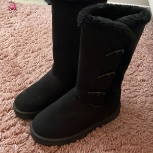 Svarta boots med päls och knäppning - Säljer ett par svarta boots med mjuk päls på insidan och längs kanten. Skorna har tre snygga knäppningar på sidan och en platt sula. Perfekta för kalla dagar och har en enkel, stilren look som passar till många outfits.