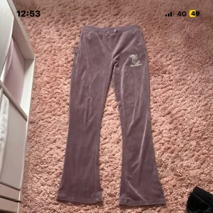 Lila velourbyxor Juicy Couture - Säljer ett par lila mjukisbyxor från Juicy Couture i mjuk velour med bootcut-ben. Byxorna har snörning i midjan, ficka bak och ett glittrigt Juicy Couture-emblem med strass på framsidan. Perfekta för en chill och trendig look.