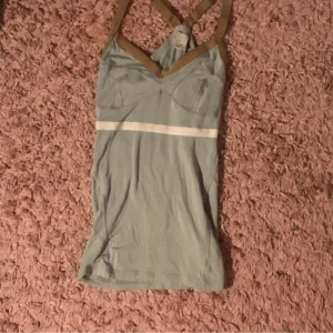 Ljusgrön linnetopp från H&M - Snygg ljusgrön linnetopp från H&M med beige axelband som korsas i ryggen och en vit horisontell rand över bröstet. Toppen är figurnära och har sömmar som markerar bysten. Perfekt för dig som gillar stilrena detaljer och enkel design.