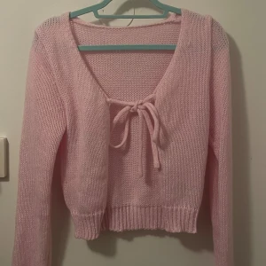 Ljusrosa stickad kofta från SHEIN - Supersöt ljusrosa stickad kofta från SHEIN med knyt framtill och v-ringad hals. Koftan är croppad med långa ärmar och ribbade muddar. Perfekt för lager-på-lager och ger en gullig vibe till din outfit.