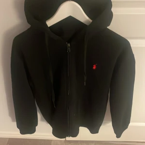 Svart hoodie från Polo Ralph Lauren - Svart hoodie från Polo Ralph Lauren med röd broderad logga på bröstet. Helt oanvänd fick den  nyss. Pris kan diskuteras 