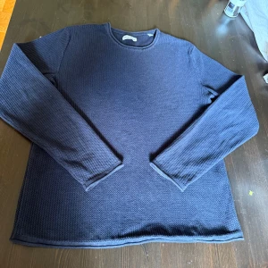 Mörkblå stickad tröja - Säljer en mörkblå stickad tröja med rund hals och långärmad design. Tröjan har en grovstickad struktur som ger en schysst textur och passar perfekt för kyliga dagar. Enkel och stilren modell som funkar till jeans eller chinos.