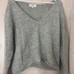 Grå stickad tröja Gina Tricot XL - Mysig grå stickad tröja från Gina Tricot i alpackablandning. Tröjan har en djup v-ringning och långa ärmar, perfekt för att hålla sig varm under kyliga dagar. Enkel och stilren design som funkar till många olika outfits. Har storlek xs men köpte xl så den är off shoulder, väldigt fin på kan visa bild kom priv