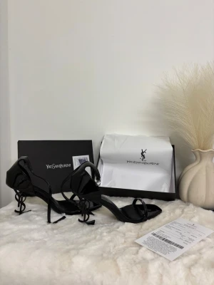 Svarta sandaler, klackar  - Säljer ett par svarta sandaler, Skorna har öppen tå, smal rem över foten och justerbart spänne vid ankeln. Riktigt statement piece för dig som gillar lyxiga detaljer och edgy design.