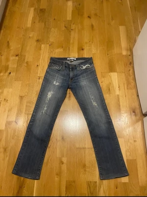J.lindberg jeans - Säljer ett par blå jeans från j.lindberg med slim/rak passform. Jeansen har slitna detaljer framtill och coola orange broderier på bakfickorna. Det står att storleken är 30/32 men skulle säga att de passar mer som 29/30