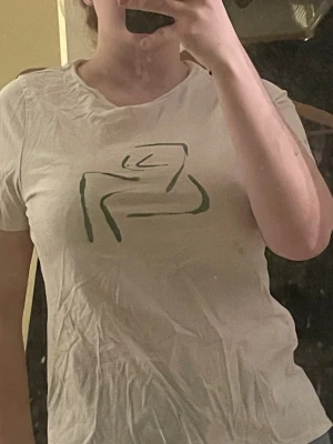 Vit t-shirt med grön print från NA-KD - Vit t-shirt från NA-KD i mjuk bomull med ett grönt abstrakt tryck framtill. Klassisk rund hals och korta ärmar. Perfekt för en chill och stilren look.