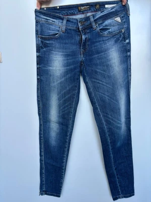 Replay Radula blå jeans, W27 L30 - Snygga blå jeans från Replay, modellen Radula. De har klassisk femficksdesign. Jeansen är tillverkade i jeansmaterial med en smal passform och normal midja. Perfekta för dig som gillar stilrena detaljer.