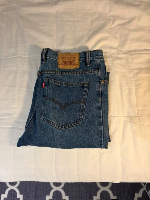 Levi's 501 blå jeans straight fit - Klassiska Levi's 501 jeans i blå denim med straight fit och hög midja. Snygga detaljer som fem fickor, knappgylf och den ikoniska läderpatchen bak. Perfekt för dig som gillar tidlös stil och vill ha ett par jeans som alltid funkar.