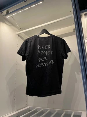 Bvaldi t-shirt med tryck  - Svart t-shirt från Bvaldi  med coolt strasstryck. Framsidan har en liten 'VIP'-logga i strass och baksidan har texten 'NEED MONEY FOR PORSCHE' i samma stil. Klassisk rund hals och korta ärmar, tillverkad i mjuk bomull. Passar till både herr och dam 