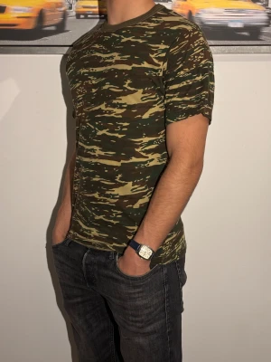 Vintage Camouflage t-shirt  - Säljer en snygg t-shirt med klassiskt camouflage-mönster i gröna och bruna toner. T-shirten har rund hals och korta ärmar, perfekt för dig som gillar streetstyle eller vill sticka ut lite extra. Materialet är mjuk bomull som känns skönt mot huden.