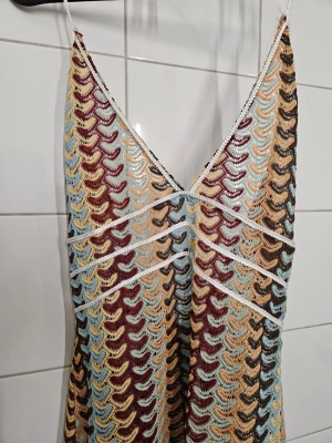 Klänning - Lång klänning för strand eller sommaren. Mönstrad och med halterneck. Den är inte heltäckande, utan mer som en beach cover-up. Det finns en dold dragkedja i sidan. Det finns ingen storlekslapp, men uppskattar den till strl M.