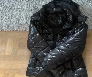 Svart pufferjacka från 157 med huva - Säljer en svart, glansig pufferjacka från 157 i storlek M. INGA HÅL helt som ny inte använt den en ända gång . 