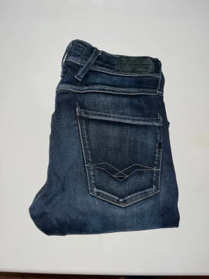 Replay Anbass jeans - Snygga Replay Anbass jeans i mörkblå tvätt med klassiska fem fickor och kontrastsömmar. Modellen har smal passform och raka ben. Tyvärr saknas storlekslappen men jag bedömer den till W30 L30 men utgå från måtten då det bara är en uppskattad storlek som ej behöver stämma :) Midja 36cm, längd 97cm. JAG SKICKAR EJ FLER BILDER NÄR JAG BÄR JEANSEN! för storleksguide hänvisar jag till måtten och för bättre inblick i passformen rekommenderar jag att googla på modellnamnet. kolla måtten noggrant :) 77