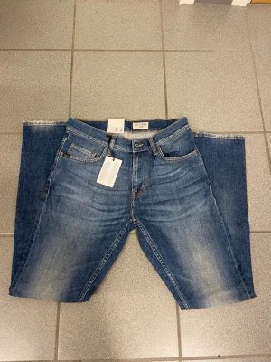 Blå tapered jeans från Tiger of Sweden  W29 L32 - Snygga blå jeans från Tiger of Sweden  med avslappnad passform och tapered ben. Jeansen har klassisk femficksdesign, bruna kontrastsömmar och läderpatch bak i midjan. Tillverkade i bomull med en tvättad look och subtila slitningar för en cool vibe.