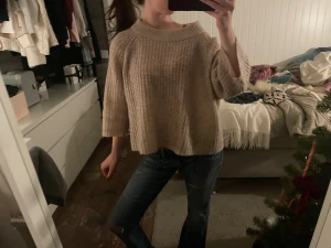 Beige stickad tröja med trekvartsärm - Säljer en beige stickad tröja med croppad passform och breda trekvartsärmar. Tröjan har en grovstickad struktur och en rund halsringning som ger en chill och avslappnad vibe. Perfekt att styla med jeans eller kjol för en cool look.