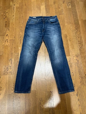 Jack & Jones Clark Regular Jeans 29/30 - Säljer ett par blå jeans från Jack & Jones, modell Clark Regular. Klassisk femficksdesign, normal passform och snyggt tvättad denim med ljusare partier. Perfekta för dig som gillar en enkel och stilren look. Materialet är jeans i bomull. Jeansen är använda några gånger men det är inga fel på dom 