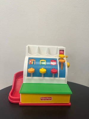 Ingen väst på bilderna - Bilderna visar ingen väst, utan en leksakskassa från Fisher Price i plast med färgerna vit, blå, grön, gul och röd.