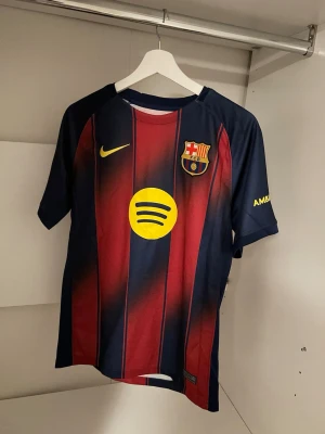 FC Barcelona Lamine Yamal matchtröja - Säljer en officiell FC Barcelona matchtröja från Nike med Lamine Yamal och nummer 10 på ryggen. Tröjan är i blått och vinrött med gula detaljer, klubbmärke på bröstet och sponsorloggor. Tillverkad i lätt polyester med Dri-FIT-teknologi för bästa komfort. Tröjan är köpt i Spotify camp nou och är äkta. Original pris 185 euro vilket motsvarar i cirka 2000 kr