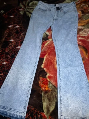 Ljusblå bootcut jeans - Säljer ett par ljusblå jeans med bootcut passform och klassisk femficksdesign. Jeansen har en snygg tvättad look och är tillverkade i jeansmaterial. Perfekta för dig som gillar retrovibbar och vill ha ett par jeans med lite extra sväng i benen.