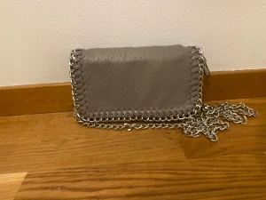 Grå axelväska med kedja - Grå väska från tiamo,den är i bra skick och bandet ingår med väskan💕