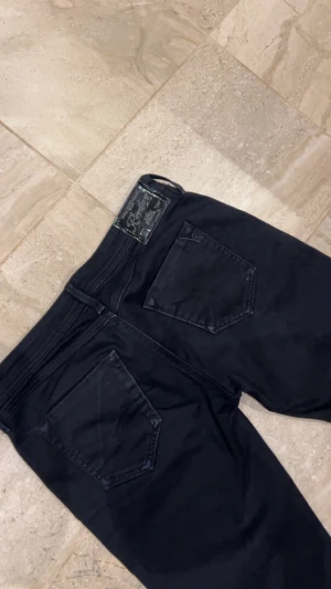 Svarta Replay jeans straight fit - Snygga svarta jeans från Replay med klassisk femficksdesign och raka ben. Jeansen har en svart läderpatch med Replay-logga bak i midjan och diskreta sömmar. Materialet är jeans med en mjuk känsla och passformen är normal med midwaist. Jeansen passar om man har stl S eller xs. 