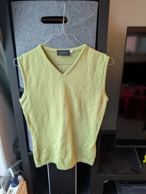 Ljusgrön stickad väst från Gianini - Snygg ljusgrön stickad väst från Gianini i storlek M. Västen har en klassisk v-ringad hals och ribbade kanter vid ärmhål och hals. Perfekt att styla över en t-shirt eller skjorta för en chill och trendig look.