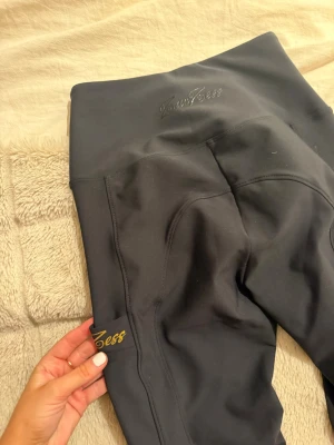 Svarta ZacZess leggings med guldtryck - Snygga svarta leggings från ZacZess med högt midjeband och guldigt logotryck på benet. Stretchigt material som sitter skönt och följer kroppen. Perfekta för träning eller chill, med stilren design och diskreta sömmar. Endast använda för plåtning.