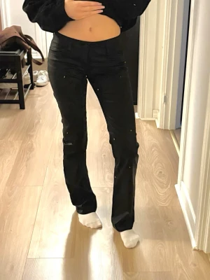Svarta lågmidjade skinnbyxor - Säljer ett par svarta skinnbyxor med lowwaist och straight fit. Byxorna har klassisk femficksdesign, bälteshällor och knappstängning. Materialet har en lätt glansig finish som ger en cool look. Passar dig som gillar stilrena och enkla plagg.