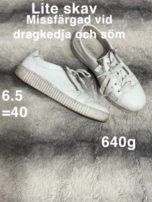 Vita sneakers från Gabor med dragkedja - Snygga vita sneakers från Gabor med coola dragkedjor på sidorna och breda vita snören. Skorna har en chunky platt sula och rund tå, perfekt för en clean och stilren look. Passar dig som gillar klassiska men ändå trendiga detaljer.🌸Sparsamt använda.ej tvättade. Lite skav. Missfärgade vid dragkedja och söm. Storlek 6.5 vilket enligt hemsidan motsvarar 40.