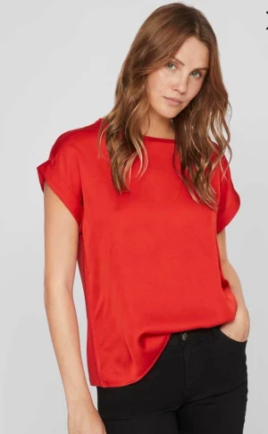 Röd satintopp från Vila, strl 34 - Snygg röd satintopp från Vila i modellen Viellette. Toppen har korta ärmar, rund halsringning och en slät, glansig finish. Perfekt att styla med jeans eller kjol för en trendig look. Färgen är poppy red och materialet känns lyxigt och mjukt.