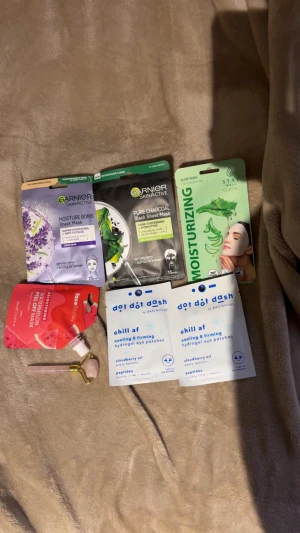 Ansiktsmasker & ögonpatches kit - Kit med flera ansiktsmasker: Garnier Moisture Bomb, Pure Charcoal, Stay Well Aloe Vera, Facedash Watermelon peel off mask samt Patchology chill af hydrogel eye patches. Inkluderar även en rosa ansiktsroller i sten och metall. Perfekt för self-care och glow.