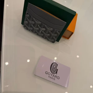 Plånbok goyardd - Supersnygg svart plånbok från G med deras ikoniska grafiska mönster i vitt och grått. Slimmad design med flera fack för kort, perfekt för dig som gillar stilrena accessoarer. plånboken kommer med certifikat kort box och även en liten påsa för förvaring. 