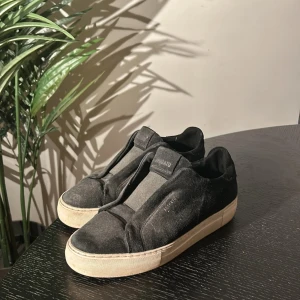 Axel arigato - Stilrena svarta sneakers från Axel arigato i mocka med en vit sula. Skorna har en minimalistisk design utan snörning. Box och dustbag kommer med, skriv vid minsta lilla fråga