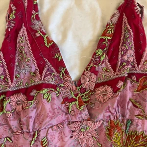 Rosa och vinröd blommig top - Supersöt top i rosa och vinrött med broderade blommor och pärlor i grönt, rosa och silver. V-ringad upptill och axelbandslös design. Materialet känns som siden eller polyester och har en lyxig känsla. Perfekt för dig som gillar detaljer och färg! Den är från en marknad i Frankrike 