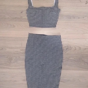 Svartvit rutig croppad linnetopp - Snygg croppad linnetopp i svartvitt rutigt mönster. Toppen har breda axelband och fyrkantig urringning, perfekt för en trendig look. Passar till både kjol och jeans för en cool outfit.