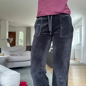 Svarta mjukisbyxor i sammet - Mysiga svarta mjukisbyxor från juicy couture i sammet med breda ben och stora fickor framtill. Byxorna har snörning i midjan och bakfickor med knappar. Perfekta för chill dagar hemma eller när du vill vara bekväm men ändå se snygg ut.