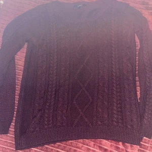 Vinröd stickad tröja från Lindex - Mysig vinröd stickad tröja från Lindex med klassiskt flätmönster och rund halsringning. Tröjan har långa ärmar och ribbade muddar vid ärmslut och nederkant. Perfekt för lager-på-lager och chill höst- och vinterstil.