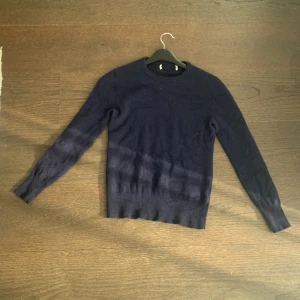 Mörkblå stickad tröja - Mörkblå stickad tröja med rundad hals och långa ärmar. Tröjan har en enkel och klassisk design med ribbad kant vid halsen. Perfekt för dig som gillar stilrena och mjuka plagg. Passar dig som vill ha en basic tröja i garderoben.från sayless