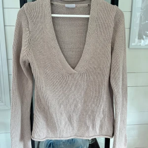 Beige stickad v-ringad tröja Boomerang - Säljer en beige stickad tröja från Boomerang med djup v-ringning och lång ärm. Tröjan är i ett mjukt material och har en enkel, clean look som passar perfekt till jeans eller kjol. Perfekt för lager-på-lager under hösten eller våren.