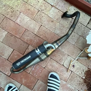 Rör - Bilden visar ett avgassystem från Tecnigas, troligen avsett för moped eller scooter. Det är ingen bok på bilden, utan en fordonsdel.