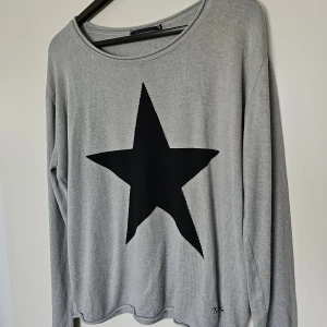 Grå stickad tröja med svart stjärna - Snygg grå stickad tröja från Bondelid i storlek M. Tröjan har en stor svart stjärna framtill som ger en cool vibe. Rund halsringning och långa ärmar. Perfekt för dig som gillar enkel men ändå unik stil. Fint skick 