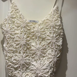 Vit spetsig croppad linnetopp Zara - Superfin vit croppad linnetopp från Zara med broderade blommor i spets och tunna axelband. Toppen har en v-ringad form och är perfekt för sommarens varma dagar. Blommönstret ger en romantisk och trendig vibe.