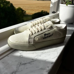 Saint Laurent skor - Snygga vita sneakers från Saint Laurent med handskriven logga på sidan. Skorna har ovandel i canvas och detaljer i skinn, klassisk snörning och platt sula. Perfekta för en clean och stilren look. Kommer med originalkartong!