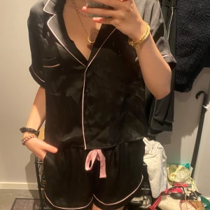 Silk pyjamas  - Säljer ett par svarta pyjamasshorts i satinliknande material med ljusrosa kantband och snörning i midjan. Shortsen har en loose fit och är perfekta för mysiga hemmakvällar. Matchar toppen med samma stil för en komplett look.
