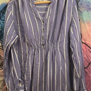 Blåvit randig blus från My Nursing Fashion - mammablus  - Säljer en blåvit randig blus från My Nursing Fashion. Blusen har v-ringning, knappar framtill och smock i midjan för en snygg passform. Långärmad och tillverkad i 100% viskos, perfekt för vår och sommar.