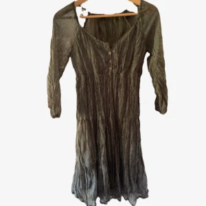 Grön klänning med småsmå blommor på❤️ - En grön klänning med trekvartsärmar och v-ringning, dekorerad med små knappar framtill. Klänningen har en skrynklig struktur och faller i en ledig passform med lätt rynkad kjol. Perfekt för dig som gillar en avslappnad och bohemisk stil.